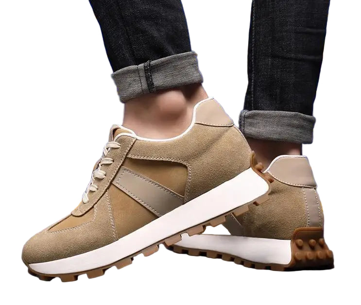 Beige sneakers with white soles worn by a person against a blue tiled wall.