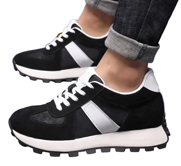 Black and white sneakers worn with rolled-up jeans on a blue floor.